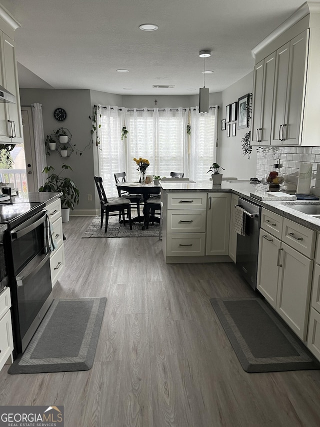 kitchen featuring a peninsula, baseboards, light wood-style floors, appliances with stainless steel finishes, and decorative backsplash