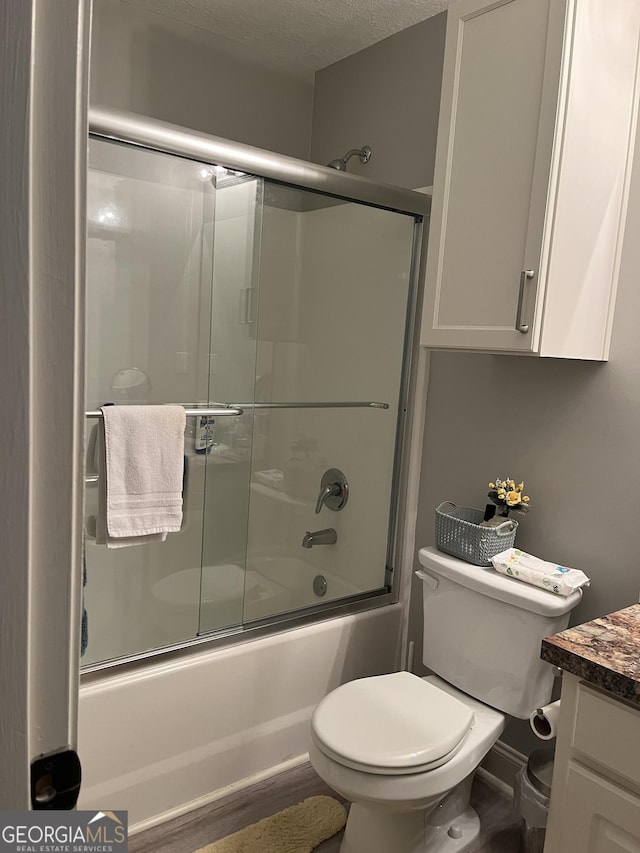 full bath with enclosed tub / shower combo, vanity, toilet, and a textured ceiling