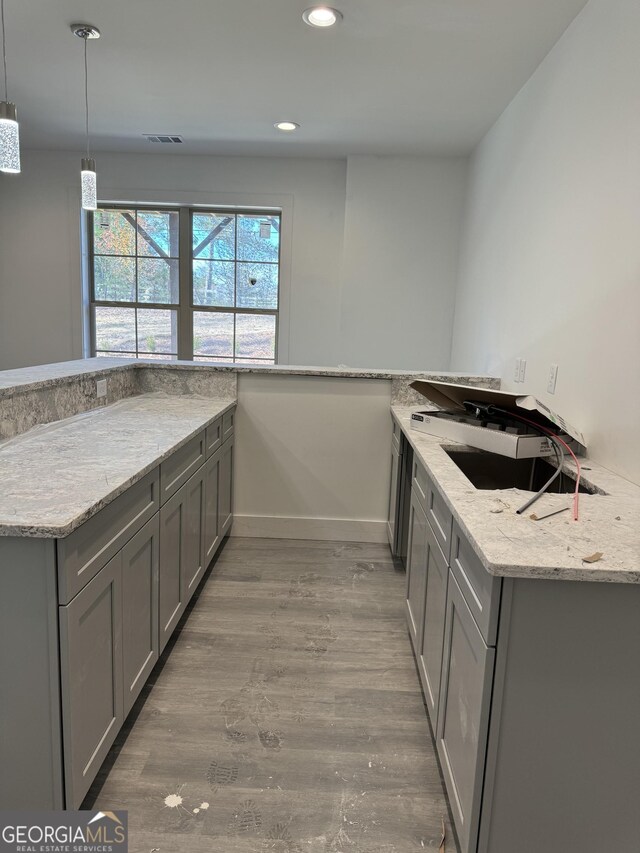 kitchen with light stone countertops, wood-type flooring, kitchen peninsula, and gray cabinetry