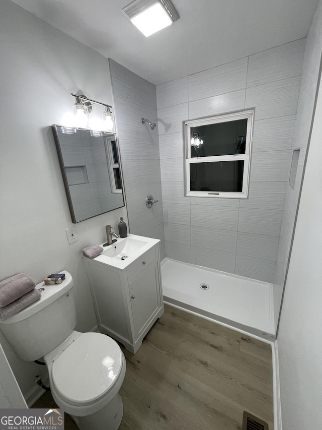 bathroom with toilet, hardwood / wood-style floors, vanity, and a tile shower