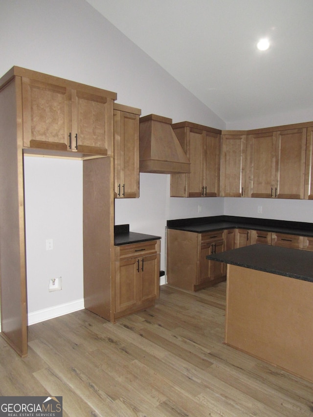 kitchen featuring light wood-type flooring, custom range hood, and vaulted ceiling