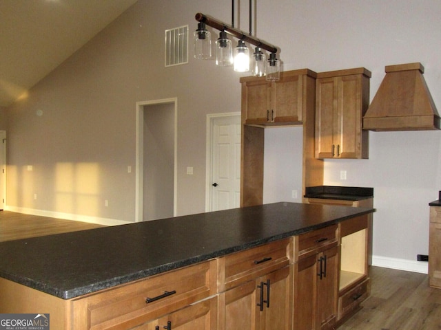 kitchen featuring pendant lighting, custom exhaust hood, lofted ceiling, dark stone countertops, and dark hardwood / wood-style flooring