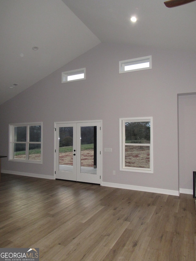 unfurnished living room featuring hardwood / wood-style flooring, plenty of natural light, high vaulted ceiling, and french doors