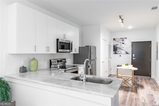 kitchen with kitchen peninsula, white cabinetry, stainless steel appliances, and light hardwood / wood-style floors