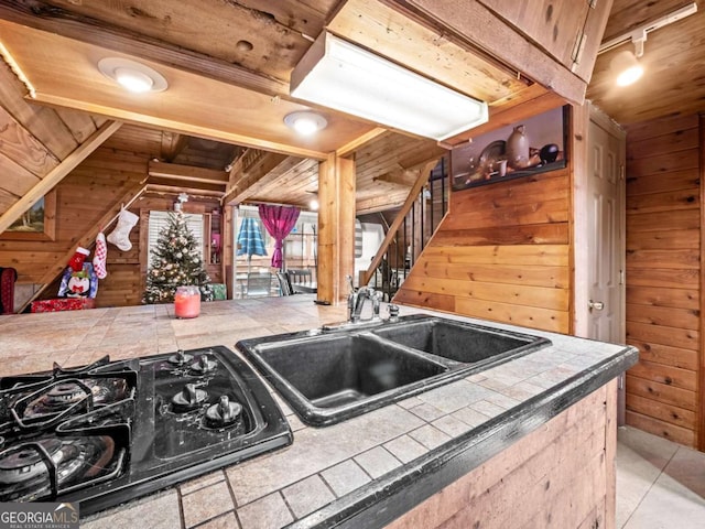 kitchen featuring sink, wood ceiling, wooden walls, tile counters, and black gas cooktop