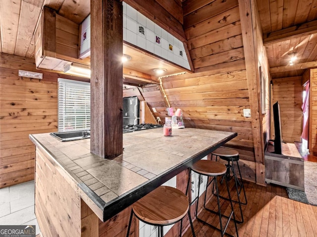 kitchen with tile counters, wood ceiling, wooden walls, and a kitchen breakfast bar