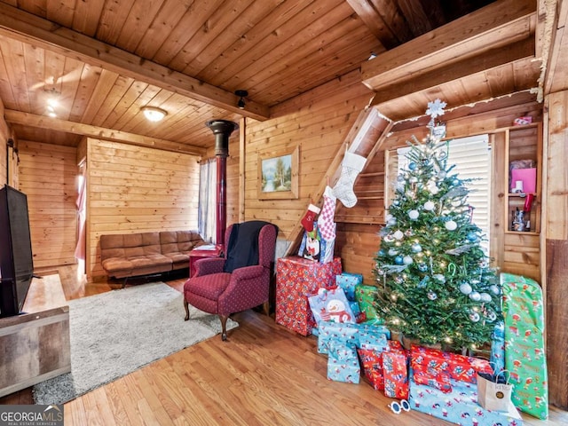 living room with a wood stove, wooden ceiling, wooden walls, beamed ceiling, and hardwood / wood-style floors