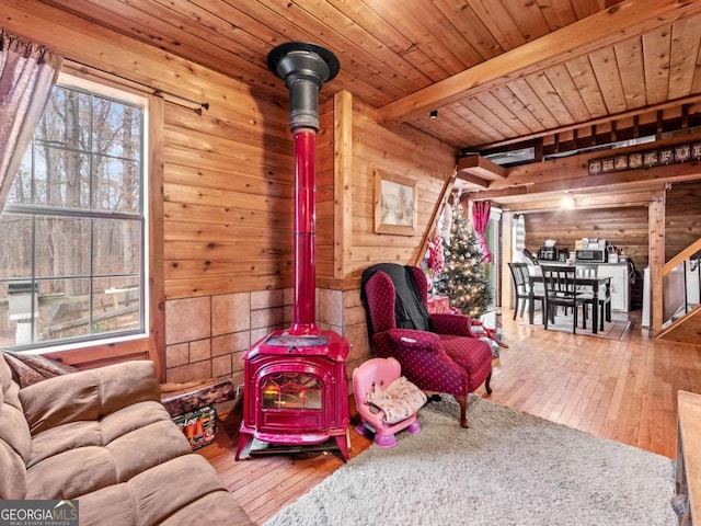 living room with hardwood / wood-style floors, wooden walls, wooden ceiling, beamed ceiling, and a wood stove