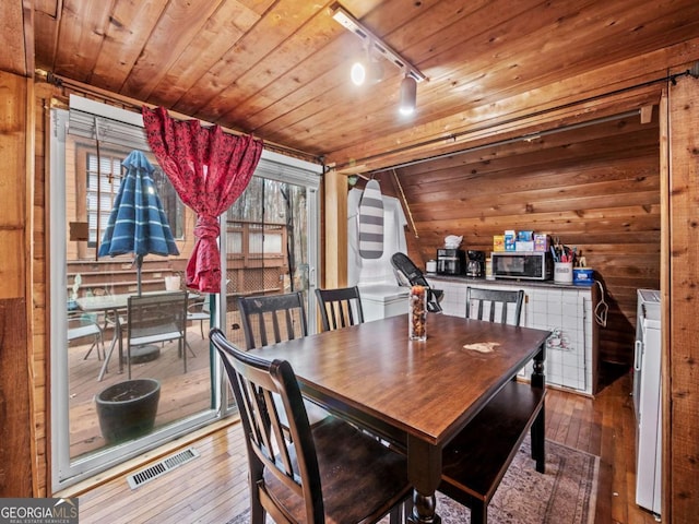 dining area featuring hardwood / wood-style flooring, rail lighting, wooden walls, vaulted ceiling, and wooden ceiling