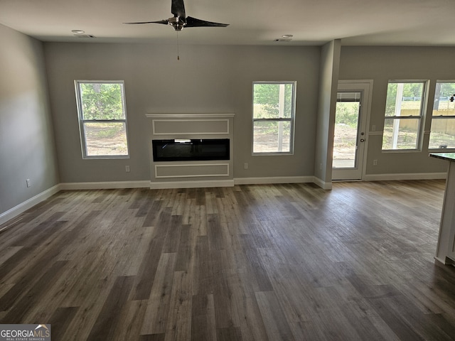 unfurnished living room with dark hardwood / wood-style flooring, a wealth of natural light, and ceiling fan