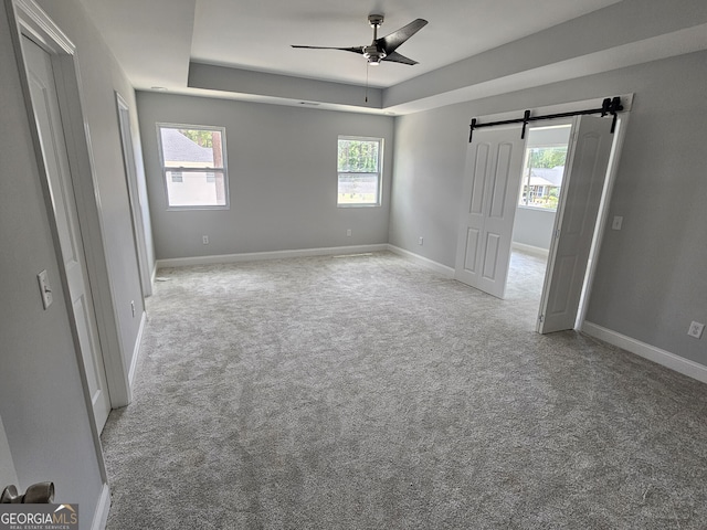 carpeted spare room with plenty of natural light, ceiling fan, and a barn door