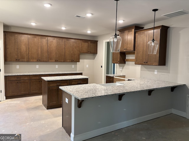 kitchen featuring kitchen peninsula, pendant lighting, a breakfast bar area, and light stone counters