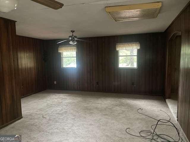 empty room with light carpet, ceiling fan, and wooden walls