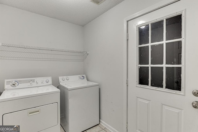 laundry area with light tile patterned flooring, a textured ceiling, and washing machine and clothes dryer