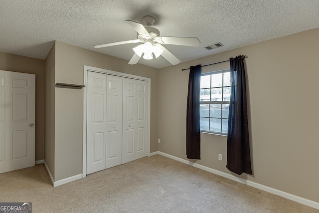 unfurnished bedroom featuring ceiling fan, a closet, light carpet, and a textured ceiling