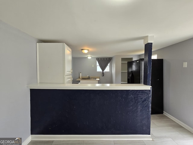 kitchen featuring kitchen peninsula, black refrigerator, white cabinets, and sink