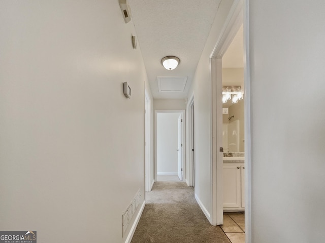 hallway with light carpet, a textured ceiling, and sink