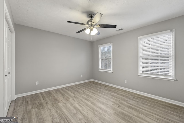 empty room with ceiling fan, light hardwood / wood-style flooring, and a textured ceiling