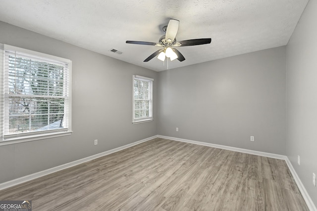 empty room with light hardwood / wood-style floors, a textured ceiling, and a wealth of natural light