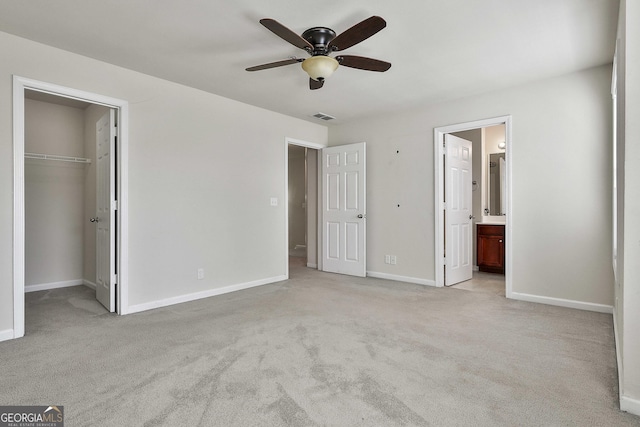 unfurnished bedroom with connected bathroom, ceiling fan, a walk in closet, light carpet, and a closet