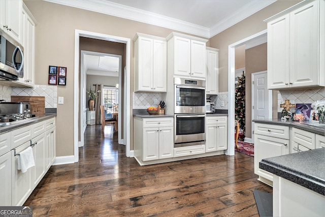 kitchen featuring dark wood-type flooring, appliances with stainless steel finishes, white cabinetry, tasteful backsplash, and ornamental molding