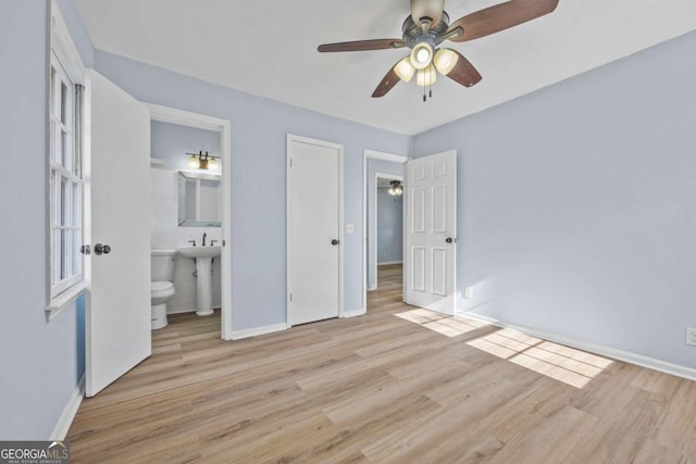 unfurnished bedroom with light wood-type flooring, ensuite bathroom, ceiling fan, sink, and a closet