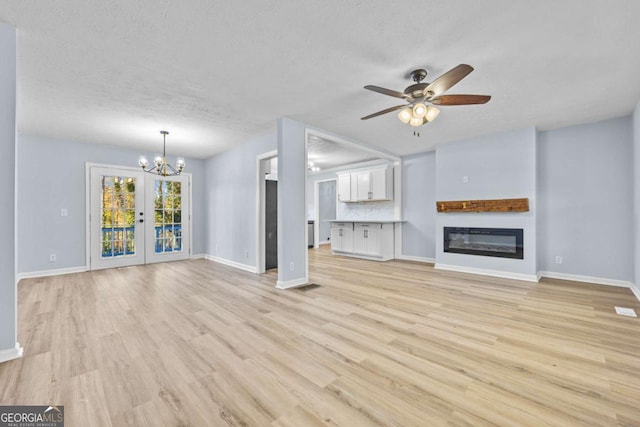 unfurnished living room with a textured ceiling, french doors, light hardwood / wood-style floors, and ceiling fan with notable chandelier