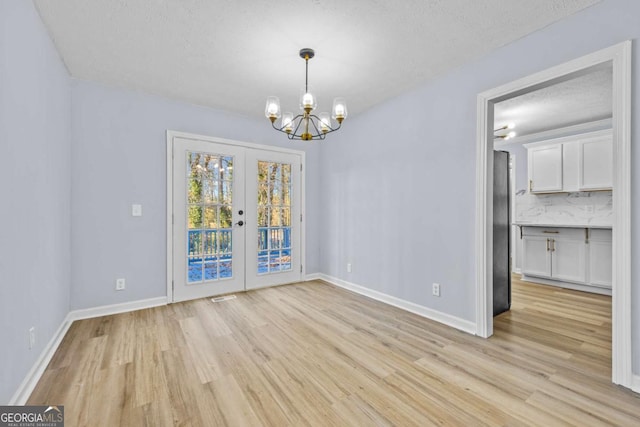 unfurnished dining area with a chandelier, french doors, light wood-type flooring, and a textured ceiling