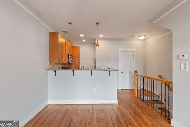 kitchen with backsplash, kitchen peninsula, hardwood / wood-style floors, decorative light fixtures, and a kitchen bar