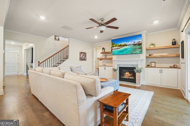 living room with a premium fireplace, ceiling fan, light hardwood / wood-style floors, and crown molding