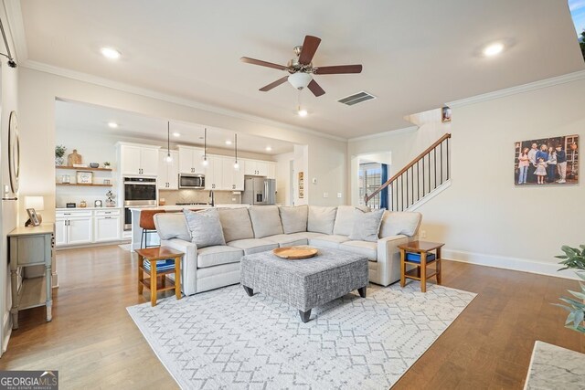 living room featuring sink, light wood-type flooring, ceiling fan, and ornamental molding