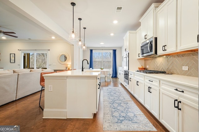 kitchen with a center island with sink, backsplash, white cabinets, appliances with stainless steel finishes, and ceiling fan