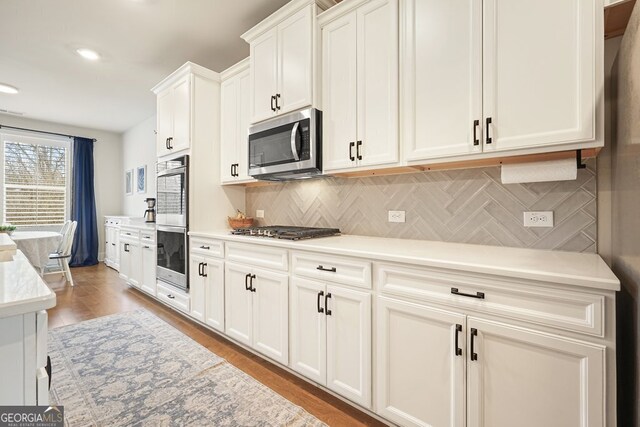 kitchen with appliances with stainless steel finishes, light hardwood / wood-style floors, white cabinetry, and decorative backsplash