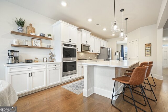 kitchen with decorative light fixtures, white cabinets, appliances with stainless steel finishes, and a kitchen island with sink