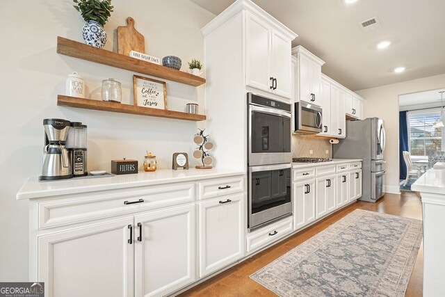 kitchen with appliances with stainless steel finishes, light hardwood / wood-style flooring, white cabinetry, and backsplash