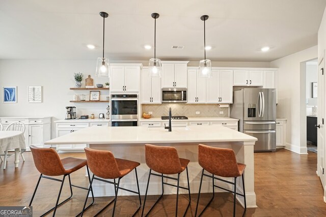 kitchen with pendant lighting, stainless steel appliances, a center island with sink, backsplash, and a kitchen breakfast bar