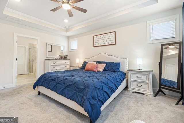 bedroom featuring a raised ceiling, ceiling fan, ornamental molding, ensuite bath, and light colored carpet