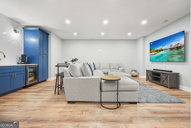 living room with beverage cooler, light hardwood / wood-style flooring, and indoor bar