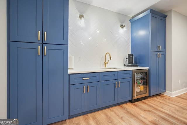 bar featuring light hardwood / wood-style floors, wine cooler, backsplash, blue cabinets, and sink