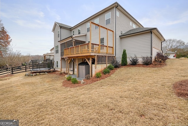 rear view of house featuring a yard, a wooden deck, a sunroom, and a trampoline