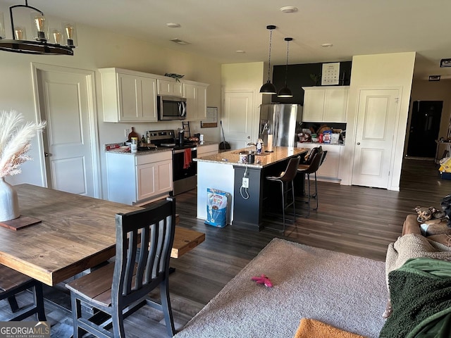 kitchen featuring a kitchen island with sink, light stone countertops, appliances with stainless steel finishes, decorative light fixtures, and a breakfast bar area