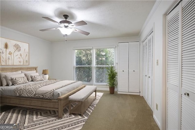 bedroom featuring multiple closets, ornamental molding, dark carpet, and ceiling fan