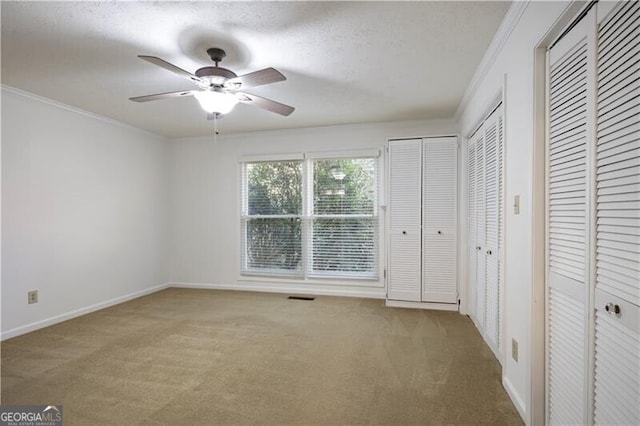 unfurnished bedroom with ceiling fan, crown molding, carpet floors, and multiple closets