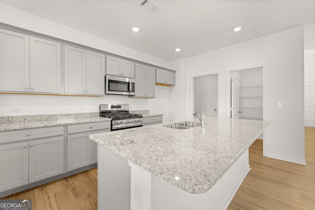 kitchen with sink, stainless steel appliances, light stone counters, light hardwood / wood-style flooring, and an island with sink