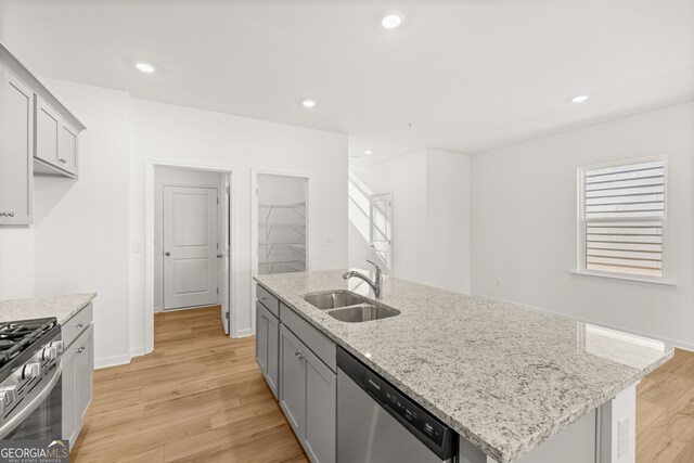 kitchen featuring appliances with stainless steel finishes, light stone counters, sink, a center island with sink, and light hardwood / wood-style flooring