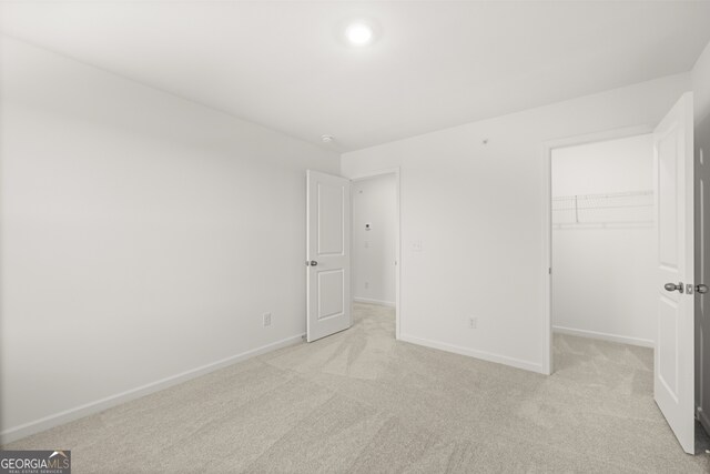 unfurnished bedroom with light colored carpet, a walk in closet, and a closet