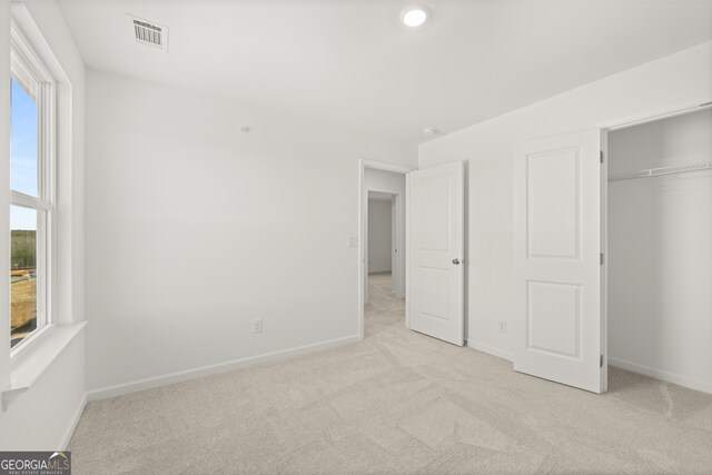 unfurnished bedroom featuring multiple windows, light carpet, and a closet