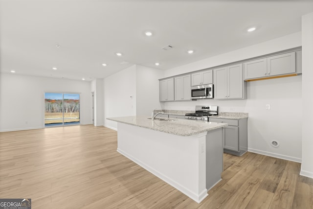 kitchen with gray cabinets, light stone countertops, stainless steel appliances, and a kitchen island with sink