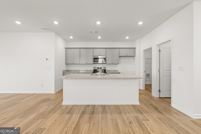 kitchen featuring appliances with stainless steel finishes, a center island with sink, and light stone counters