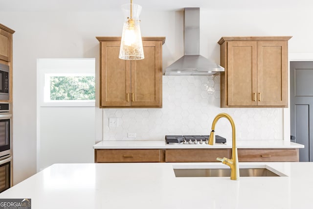 kitchen with sink, wall chimney exhaust hood, hanging light fixtures, stainless steel appliances, and tasteful backsplash